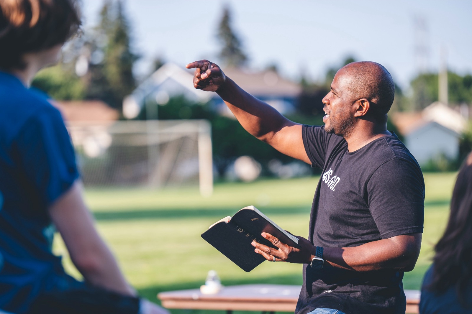 A man holding an open Bible, teaching a group outdoors
